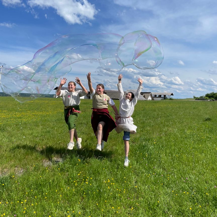 Kinder springen über eine grüne Wiese im Außenbereich der Heuneburg – Stadt Pyrene. 