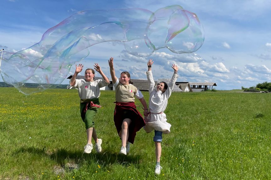 Kinder springen über eine grüne Wiese im Außenbereich der Heuneburg – Stadt Pyrene. 
